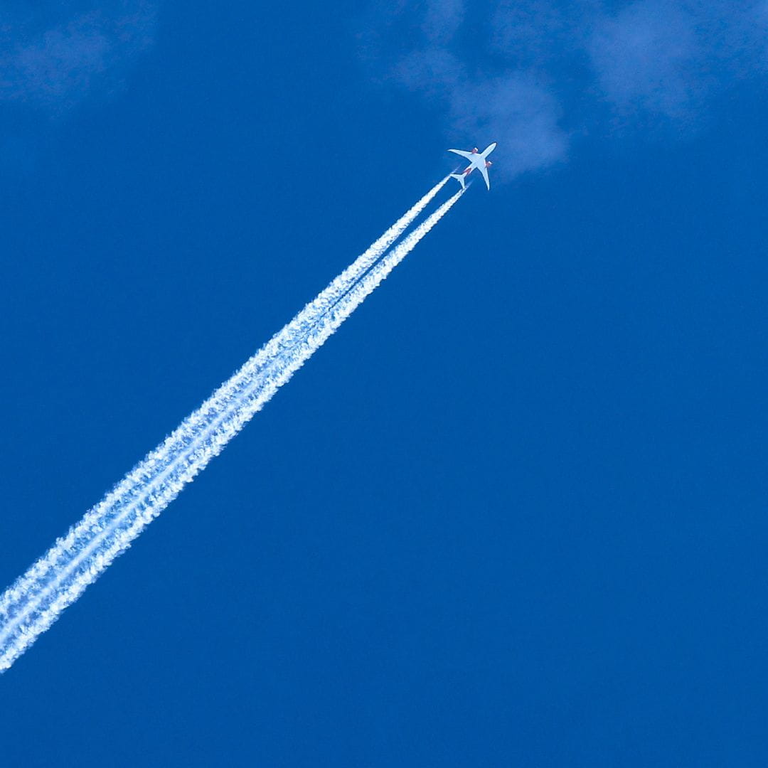 Commercial airliner at cruising altitude leaving a white contrail across a nearly cloudless blue sky.
